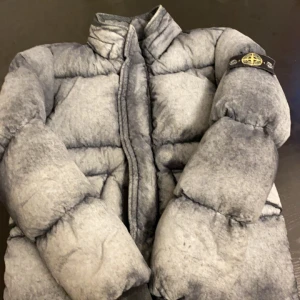 Grå Stone Island puffer - Säljer nu denna Stone Island jackan då den är alldeles för liten. Den är i fint skick använd ett fåtal. Den är en eftertraktad modell då den ändrar färg från mörkgrå till ljusgrå beroende på ifall det är kallt eller varmt. Ny pris 6000. Pris kan diskuteras vid snabb affär!