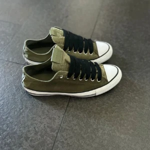 Olivgröna sneakers från Converse - Säljer ett par olivgröna Converse sneakers i bra skick. De har en klassisk design med svart snörning och vit tåhätta. Perfekta för vardagsbruk och ger en avslappnad stil. Passar bra till både jeans och shorts!