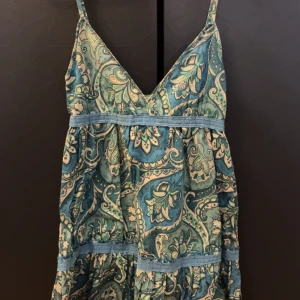 Mönstrad klänning från Amisu - Säljer en superfin mönstrad klänning från Amisu i storlek 34. Den har ett vackert paisleymönster i blå och gröna toner med smala axelband och en v-ringad design. Perfekt för sommardagar eller en avslappnad fest. Klänningen är i mycket bra skick och redo för nya äventyr!