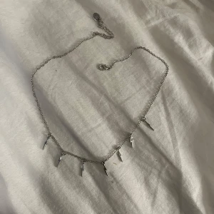 Silverfärgat halsband med blixtberlocker - Säljer ett snyggt silverfärgat halsband med små blixtformade berlocker. Perfekt för att ge en cool touch till din outfit. Halsbandet är justerbart i längd och passar till både vardag och fest. Ett måste för dig som gillar unika smycken!