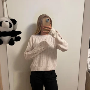 Vit stickad tröja med knappar - Säljer en superfin ljusrosa stickad tröja med unika knapplister på ärmarna. Perfekt för kyliga dagar och passar både till vardags och lite finare tillfällen. Tröjan har en normal passform och är riktigt mysig att ha på sig. Perfekt för höst och vinter!