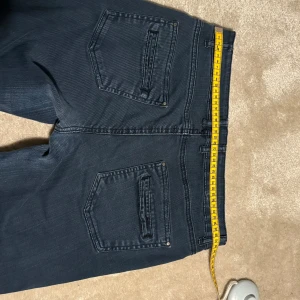 Mörkblå jeansbyxor - Säljer ett par mörkblå jeansbyxor i bra skick. De har en klassisk femficksdesign med två bakfickor och tre framfickor. Byxorna har en knapp och dragkedja framtill. Perfekta för vardagsbruk och kan matchas med nästan vad som helst. Passar både till avslappnade och mer uppklädda tillfällen.