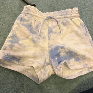 Mönstrade shorts från Lindex - Säljer ett par supercoola shorts från Lindex i storlek 134/140. De har ett unikt mönster i blått och beige med en bekväm resårmidja och snörning. Perfekta för sommarens alla äventyr! 🩳✨