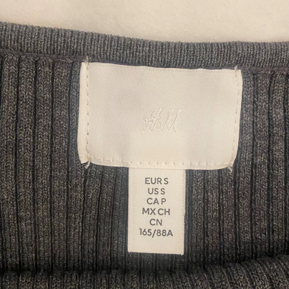 Säljer en stilren grå ribbad tröja från H&M i storlek M. Tröjan har långa ärmar och en snygg detalj med pärlor längs halsringningen. Perfekt för både vardag och fest! 🖤. Neuletakit & Villapaidat.