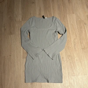 Grå ribbad klänning - Säljer en stilren grå ribbad klänning med långärmad design. Perfekt för både vardag och festliga tillfällen. Klänningen har en tight passform som framhäver figuren och är gjord i ett mjukt och bekvämt material.