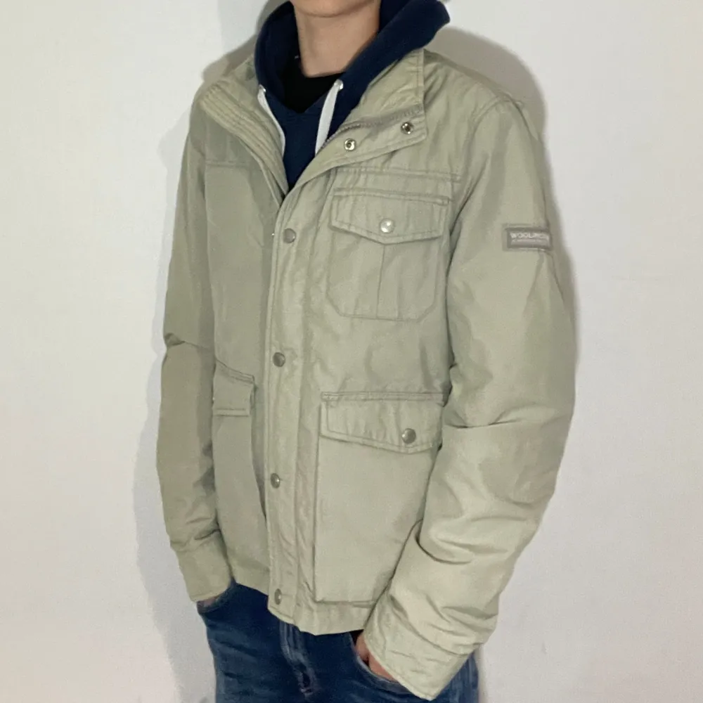 Säljer en snygg beige jacka från Woolrich i mycket bra skick. Jackan har en stilren design med knappar och dragkedja framtill. Perfekt för höst och vår och passar både till vardags och lite finare tillfällen. Modellen i bilden är 170cm lång och den sitter lite stort. Pris går att diskuteras. Jackor.