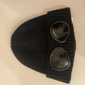  mössa från C.P. Company - Säljer en svart ribbad mössa från C.P. Company. Den är i bra skick om man bortser från den lilla slitningen på ena glaset. Passar perfekt till vintern. Priset är inte hugget i sten👍