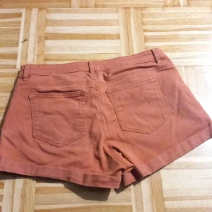 Orange shorts från H&M - Säljer ett par snygga orange röda shorts från H&M i storlek 38. De är i bra skick och perfekta för sommaren. Shortsen har en normal passform med fickor både fram och bak. Perfekta för en avslappnad dag i solen! ☀️