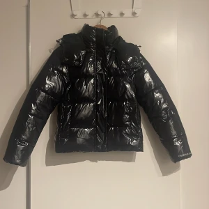Svart glansig dunjacka från Calvin Klein Jeans - Säljer en en super snygg glansig vinter jacka från Calvin Klein. Den är använd en säsong med inga defekter, säljer den då den är för kort i armarna på mej.