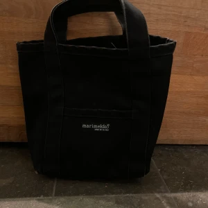 Svart väska från Marimekko - Säljer en stilren svart väska från Marimekko. Perfekt för vardagsbruk med ett enkelt och klassiskt utseende. Väskan har två handtag och är i mycket bra skick. Passar till alla säsonger och outfits!