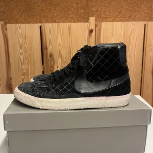 Svarta Nike sneakers med rutigt mönster - Säljer ett par svarta Nike sneakers i storlek 40. Skorna har ett coolt rutigt mönster i sammet och är i mycket bra skick. De har snörning och en vit sula som ger en snygg kontrast. Passar både tjejer och killar. Köpta i London för 10 år sedan