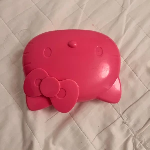 Rosa Hello Kitty box - Söt rosa Hello Kitty box i form av Hello Kittys ansikte. Den har en rosett på sidan och öppnas som ett litet etui. Perfekt för att förvara småsaker eller som en rolig accessoar. Den är vintage och har funnits massa år (Sedan 2014) 🐈‍⬛🎀 