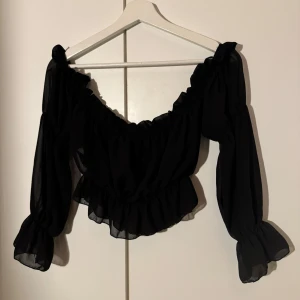 Svart blus med volangdetaljer - Säljer en elegant svart blus med volangdetaljer. Den har långa ärmar och en vacker, luftig design som passar perfekt för både fest och vardag. Blusen är i mycket bra skick och ger en romantisk touch till din outfit. Perfekt för höst och vår!