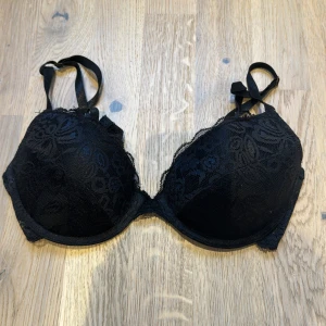 Svart spets-bh - Snygg svart bh med spetsdetaljer och justerbara axelband. Den har en klassisk design med hakknäppning bak och ger bra stöd. Perfekt för både vardag och fest! Storlek 75 C🩷