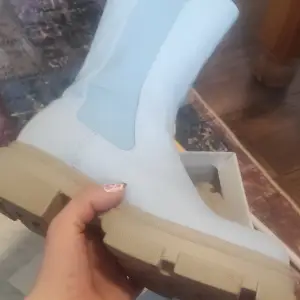 Säljer ett par ljusblå boots i syntetmaterial med en rejäl beige sula. Perfekta för att ge din outfit en cool touch. De är i bra skick och passar perfekt för höst och vår. Skorna har en stilren design utan snörning. Den har blivit skrapad på ena skon. Det är därför den säljs så billigt. Den har blivit använd endast 2 ggr