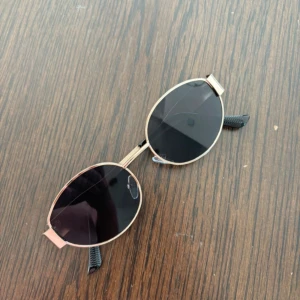 Ovala solglasögon med guldfärgad ram - Snygga ovala solglasögon med en stilren guldfärgad ram och mörka linser. Perfekta för en solig dag och ger en cool retrovibe. Passar både till vardags och festliga tillfällen. Ett måste för sommaren! Aldrig använda 