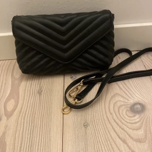 Svart axelrems väska i svart! Från Kappahl (sänkt pris!) - Säljer en snygg svart quiltad axelväska i mycket bra skick. Köpt för ca 250 kr på Kappahl och den är i mycket bra skick!💕 passar perfekt för att ha plånbok, smink och mobilen då den även har ett litet fack till på insidan! Du kan välja att ha den långa rämmen på eller hålla den med handen! Den är även justerbar vid längd!💕
