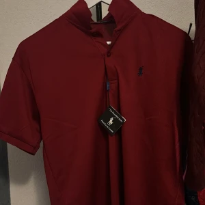 Vinröd pikétröja från Polo Ralph Lauren - Säljer en snygg vinröd pikétröja från Polo Ralph Lauren. Den har en klassisk design med korta ärmar. Aldrif använd eftersom du ser att taggen är kvar.