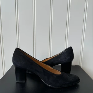 Svarta mockapumps från rizoo - Snygga svarta pumps i mocka från Rizzo De har en klassisk design med spetsig tå och en stabil klack som ger en elegant look. Perfekta för både fest och mer formella tillfällen. Skorna är i mycket bra skick och redo att användas för att komplettera din outfit.