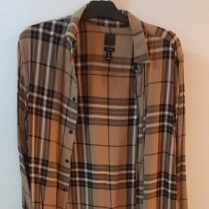 Rutig beige och brun skjorta - Säljer en snygg rutig skjorta från H&M i beige och bruna toner. Skjortan har långa ärmar och knappar framtill. Perfekt för höst och vår, och funkar både till vardags och fest. Den är i bra skick och passar perfekt för en avslappnad stil.