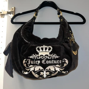 Väska från Juicy Couture - Äkta handväska i sammet från Juicy Couture 🖤Väskan har en rosett på sidan och en guldfärgad medaljong med texten 'Royal Juicy' samt ett svart hjärta på andra sidan. Dragkedjan är i guld och väskan är rymlig och i väldigt bra skick. Kan absolut förhandla priset! 