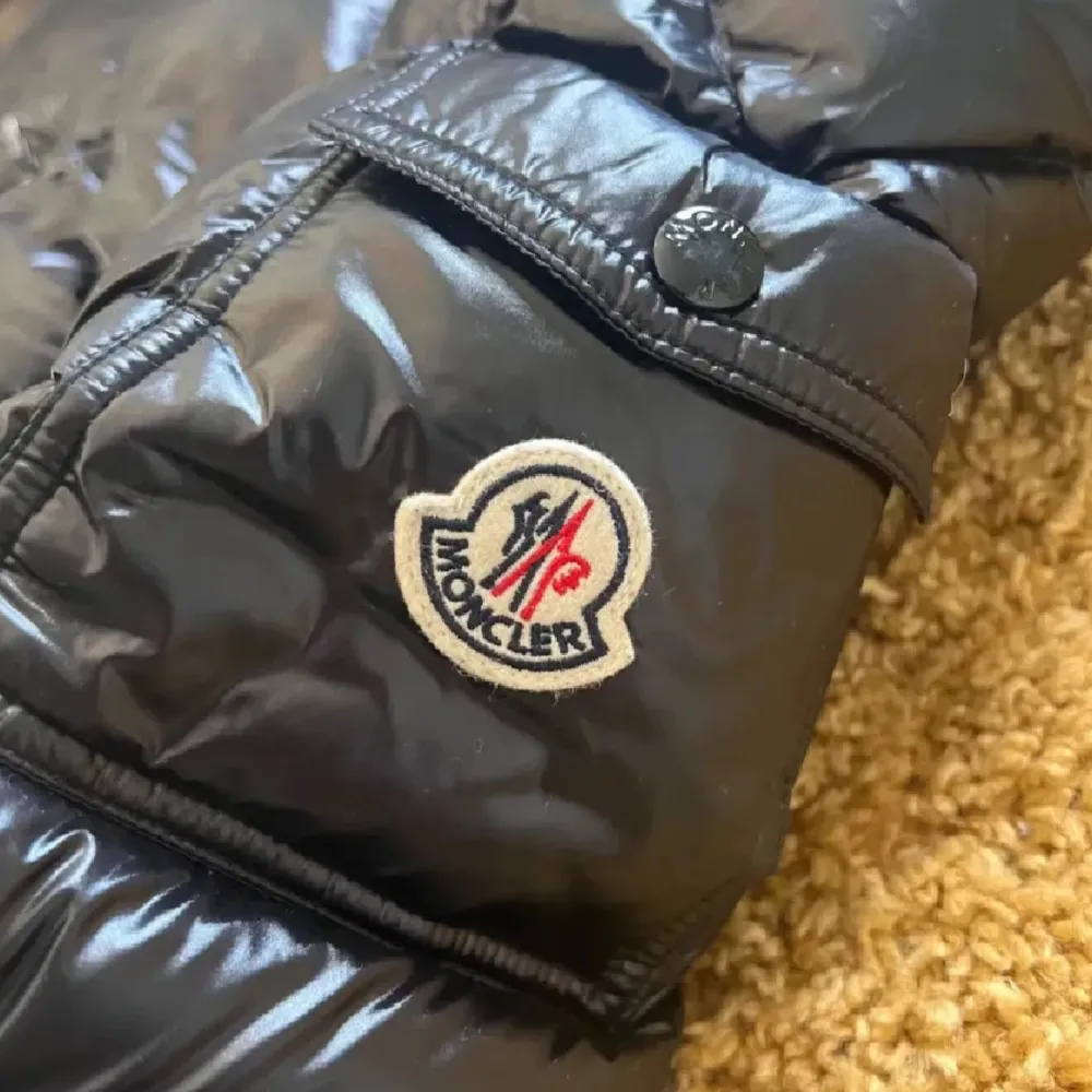 Säljer en snygg svart pufferjacka från Moncler i mycket bra skick. Jackan har en glansig finish och en praktisk huva. Den är perfekt för kalla dagar och har en dragkedja framtill. Moncler-loggan syns tydligt på armen. Passar perfekt för vintern!. Jackor.