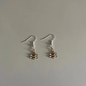 Söta bi-örhängen - Supergulliga örhängen med små bi-berlocker i gult och svart. De har vita vingar och hänger på en silverfärgad krok. Perfekta för att lägga till en lekfull touch till din outfit. Passar både till vardags och fest!