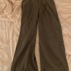 Lowwaist kostymbyxor - Säljer ett par snygga rutiga byxor i beige och svart. De har en klassisk straight passform och är perfekta för både vardag och fest. Byxorna är i mycket bra skick och har en stilren look som passar till det mesta. Perfekta för höst och vår!