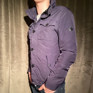 Fodrad jacka - J.Lindeberg - Säljer en snygg mörkblå jacka från J.Lindeberg i storlek M. Jackan har en stilren design med knappar och dragkedja framtill. Dragkedjan är dock trasig men den knäpps istället snyggt med knapparna som på bilden. Vid minsta fråga eller fundering hör av er🤝