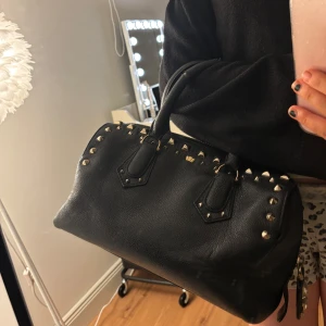 Svart handväska med nitar - snygg handväska, många fickor inuti och rymmer mycket!! slitna handtag, men annars inga defekter, bara lite sliten. 