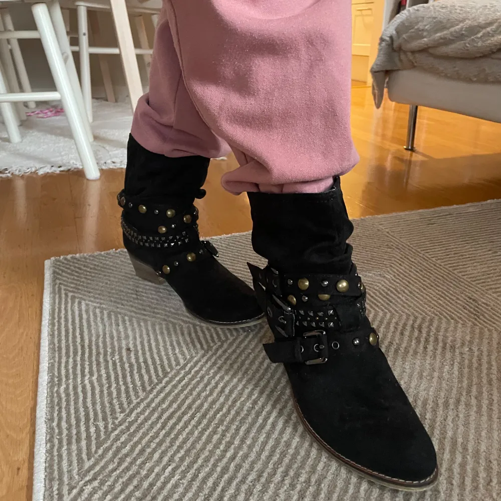 Säljer ett par svarta boots i mocka med coola nitar och spännen. De har en låg klack och är perfekta för höst och vinter. Passar både till vardags och festliga tillfällen. Skorna är i bra skick och redo för nya äventyr!. Kengät.