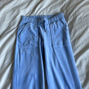 Blå byxor från Juicy Couture - Säljer ett par superbekväma ljusblå mjukisbyxor från Juicy Couture i storlek XS. De har en elastisk midja med snörning och fickor både fram och bak. Tyget har hoppat ur från metallringarna i midjan, men det är lätt att fixa. Använda ett fåtal gånger 🩵
