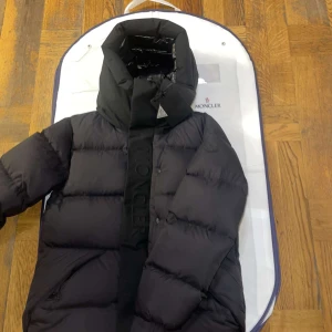 Svart dunjacka från Moncler - Säljer en snygg och varm svart dunjacka från moncler perfekt för kalla vinterdagar. Den är i nyskick aldrig använd och har en stilren design med dragkedja och knappar. Passar perfekt för både vardag och festliga tillfällen. Ända orsaken är det lilla hålet som man inte lägger märke till alls annars är den i nyskick. Pris kan diskuteras vid snabbaffär. 