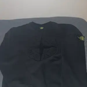 Säljer en svart tröja från Stone Island i mycket bra skick. Den har en snygg broderad logga på bröstet och en ikonisk patch på ärmen. Perfekt för höst och vinter, med en normal passform och långa ärmar. En stilren och tidlös design för alla tillfällen. Storlek M passar mer XS/S