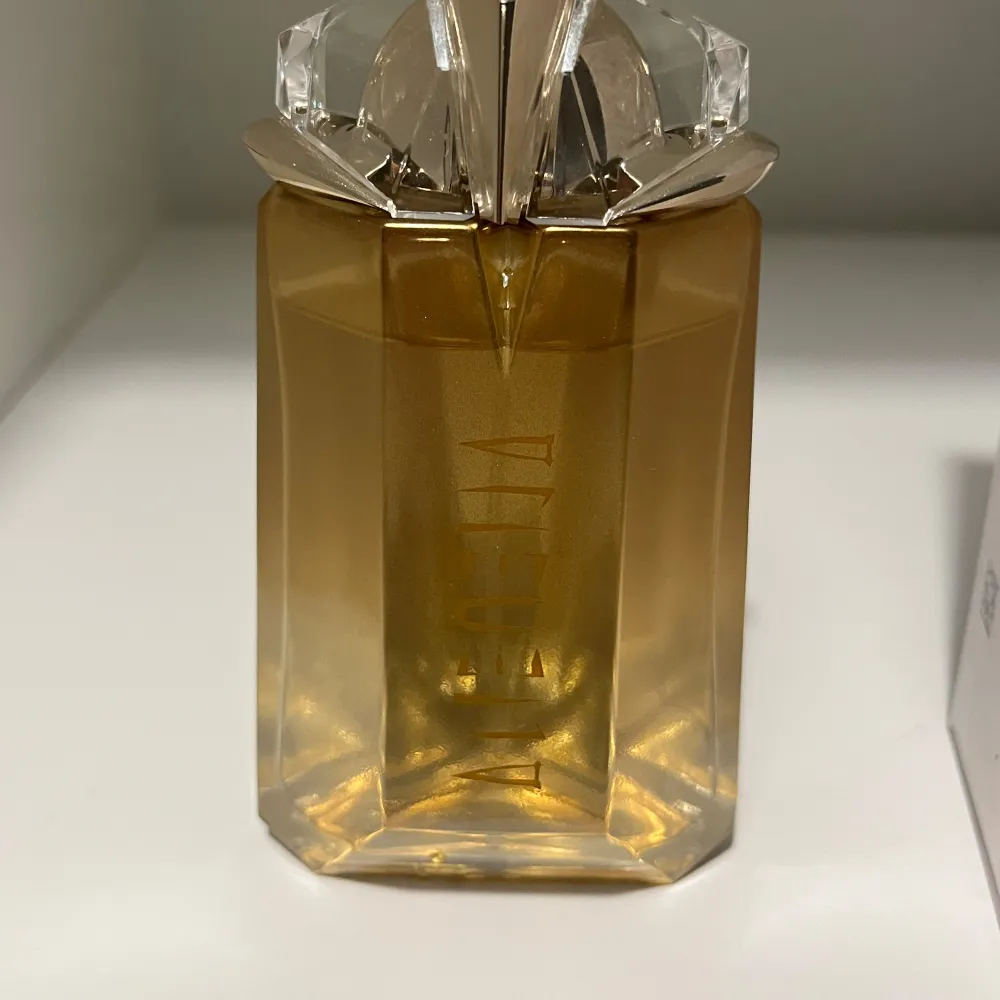 Säljer en lyxig Alien Goddess Eau de Parfum från Mugler. Flaskan är i en elegant guldton med en unik, futuristisk design. Den är påfyllningsbar och rymmer 60 mL. Perfekt för den som vill ha en doft som sticker ut och känns exklusiv. Passar både till vardags och fest!. Perfume.