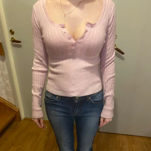 Rosa ribbad tröja med knappar - Säljer en superfin rosa ribbad tröja med lång ärm och knappar framtill. Den är figursydd och sitter snyggt på kroppen. Passar perfekt till jeans eller kjol för en avslappnad men stilren look 👚