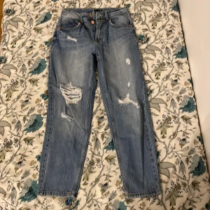 Blå jeans från Amisu - Säljer ett par snygga blå mom jeans från Amisu i storlek EU 34. De har en cool slitning på framsidan och är i bra skick. Perfekta för en avslappnad stil och passar till alla tillfällen. Högmidjade och med en bekväm passform. Kontakta mig för mer info! 💙