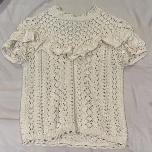 Vit stickad tröja med volangdetaljer - Superfin vit stickad tröja med korta ärmar och volangdetaljer över bröstet. Perfekt för vår och sommar! 
