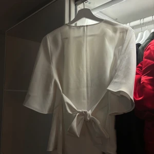 Vit blus från Zara - Säljer en stilren vit blus med knytning i bak från Zara i storlek XS. Använd en gång 