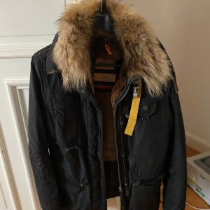 Svart jacka med pälsdetaljer - Säljer en svart jacka med snygg pälsdetalj på kragen. Jackan har långa ärmar och flera fickor med knappar. Perfekt för kyliga dagar och har en stilren look. Passar bra till både vardag och lite finare tillfällen.