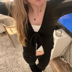 Svart omlottopp med knyt - Säljer en snygg svart omlottopp med knyt i midjan. Perfekt för både vardag och fest! Toppen har långa ärmar och en stilren design som passar till allt. Den är i bra skick och superbekväm att ha på sig. Passar perfekt till jeans eller kjol. 🖤