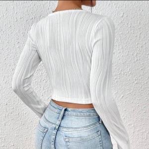 Vit ribbad croppad topp - Säljer en superfin vit ribbad topp med lång ärm och fyrkantig halsringning. Den är croppad och passar perfekt till både vardag och fest. Toppen är i mycket bra skick och ger en stilren look. (Modellbilder)