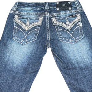 Miss Me Jeans - Miss Me jeans med bootcut-stil och strassdetaljer på bakfickorna. De har en cool tvättad look och är perfekta för en avslappnad men ändå stilren outfit. Passar bra till både vardag och fest!