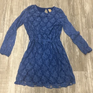 Blå spetsklänning - Säljer en superfin blå spetsklänning med långärmad design. Klänningen har en vacker öppen rygg och är perfekt för både fest och vårens tillställningar. Den är i mycket bra skick och har en normal passform. Perfekt för dig som vill ha något elegant och stilrent!