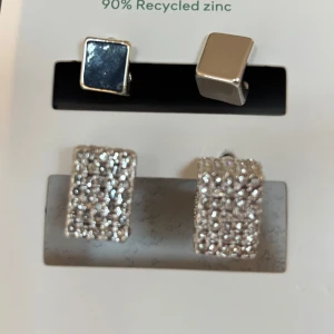 Set med fyrkantiga örhängen i återvunnet zink - Snyggt set med två par fyrkantiga örhängen i silverfärg. Det ena paret är släta och stilrena, medan det andra paret är glittriga med små stenar för extra bling. Perfekt för både vardag och fest! Tillverkade av 90% återvunnet zink.
