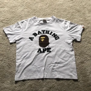 Vit t-shirt från A Bathing Ape bape - Säljer en vit t-shirt från A Bathing Ape i storlek M. Den har det ikoniska BAPE-trycket på framsidan och är gjord av 100% bomull. Perfekt för en avslappnad stil! Passar dig som är ca 176 men inte mer. För mer bilder eller funderingar skriv gärna! (Pris kan diskuteras)
