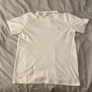 Vit t-shirt från Calvin Klein - Säljer en stilren vit t-shirt från Calvin Klein. Den är kortärmad och har en liten 'ck'-logga på bröstet. Perfekt för en avslappnad och snygg look. Passar till allt och är superbekväm!