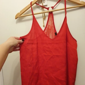 Röd spetsdetaljerad topp från BikBok - Säljer en snygg röd topp från BikBok i storlek XS. Toppen har tunna axelband och en v-ringad design med spetsdetaljer på ryggen. Perfekt för festliga tillfällen!