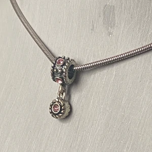 Silverhalsband med rosa stenar - Säljer ett elegant silverhalsband med en vacker hängande detalj. Halsbandet har en fin ormlänk och en charm med rosa stenar som ger en lyxig känsla. Perfekt för både vardag och fest!
