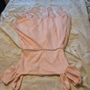 Ljusrosa glittrig klänning - Säljer en superfin ljusrosa klänning med glittrigt material. Den har en tight passform och är axelbandslös med en snygg detalj av en glittrig bård i midjan. Perfekt för fest eller bal! 💖